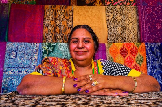 a woman sitting in front of a display of colorful fabrics
